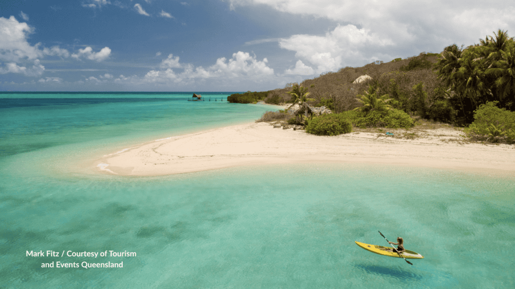 Haggerstone Island Queensland white sand spit and turquoise lagoon with a kayaker in the foreground and tropical bush behind the beach