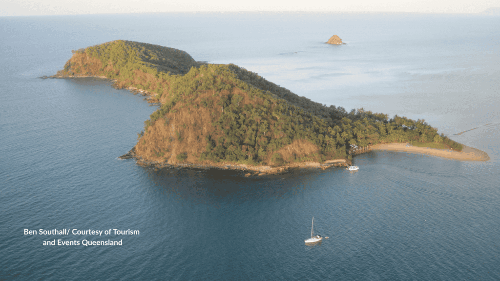 Title: Double Island Palm Cove aerial with beach and anchored boats Alt text: Aerial view of Double Island off Palm Cove Queensland with the forested hill, sandy spit and boats anchored in the bay