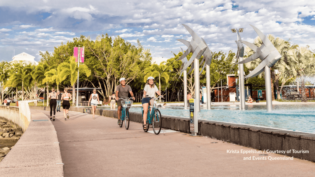 Cyclists and walkers on the Cairns Esplanade Queensland path beside the lagoon with water spraying from the bird sculptures