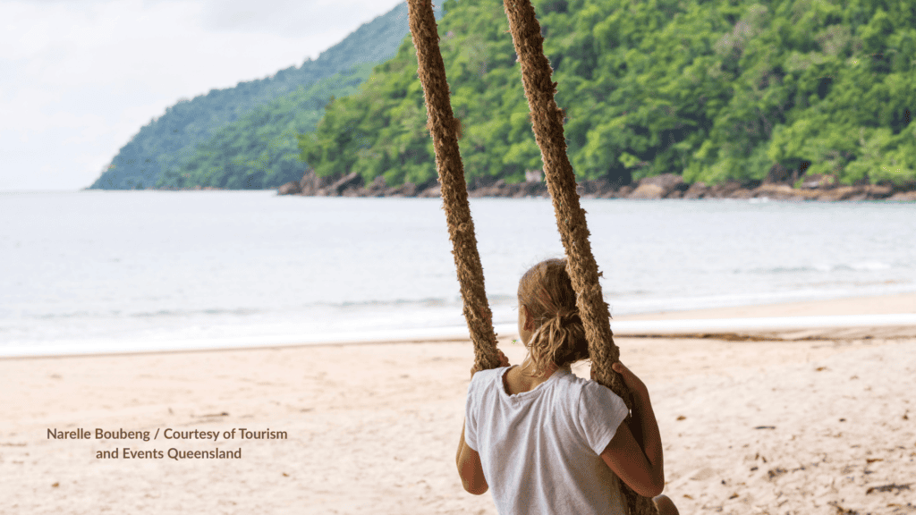 Girl on a rope swing looking out over the white sand and rainforest headland at Etty Bay Beach Innisfail Queensland