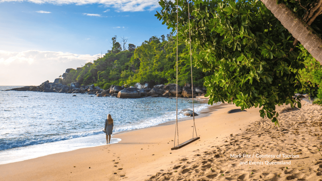 Woman walking along the sand at Bedarra Island near Mission Beach Queensland with a rope swing granite rocks and rainforest