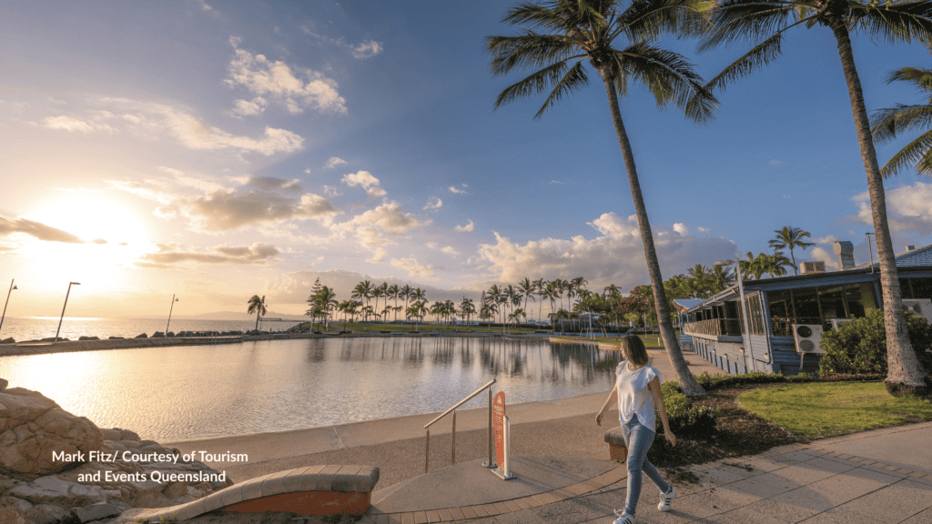 Woman walking beside the rock pool on The Strand Townsville Queensland at sunset with Magnetic Island in the distance