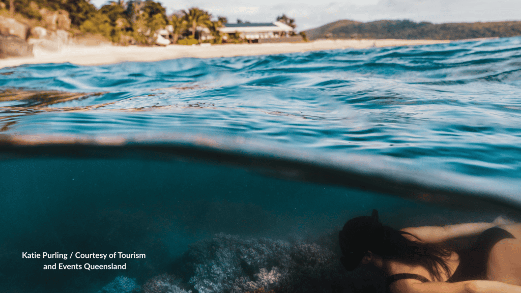 Woman snorkelling over coral off Pelorus Island near Townsville Queensland with the beach and villa above the water