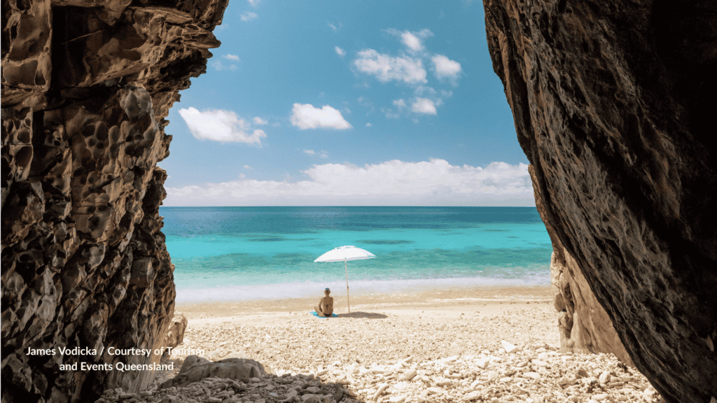 View from a cave of a person sitting under an umbrella on the beach at Orpheus Island near Townsville Queensland