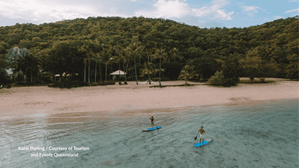 Two people stand up paddleboarding in front of the resort beach at Orpheus Island near Townsville Queensland