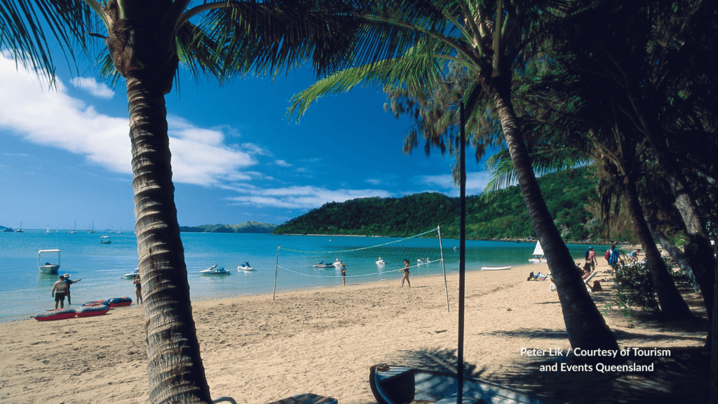 Palm framed sandy bay on Long Island Whitsundays Queensland with a volleyball net jet skis and boats offshore