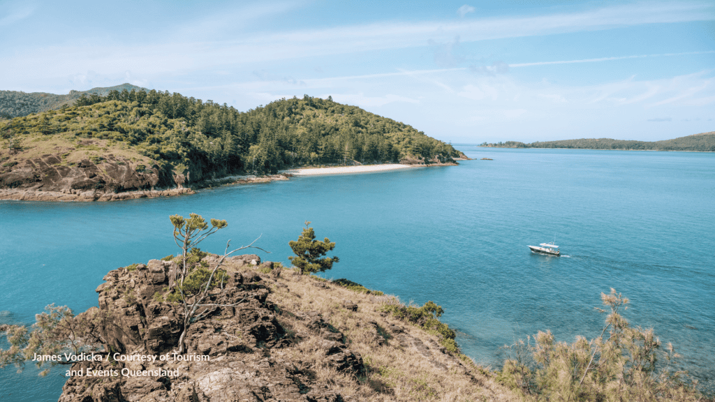 Sandy bay on Lindeman Island Whitsundays Queensland seen from a rocky headland with a boat offshore