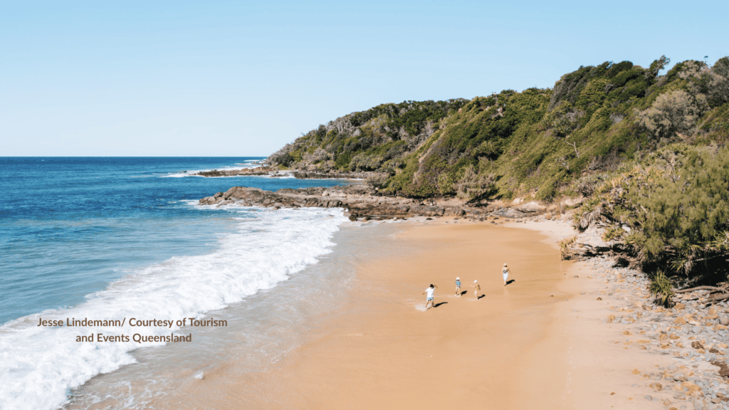 Family walking the sand at Coolum Beach Sunshine Coast Queensland beside the rocky headland and breaking waves