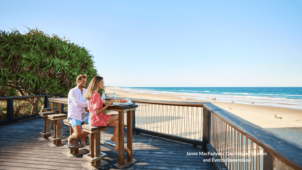 Couple dining on a timber deck overlooking Coolum Beach Sunshine Coast Queensland and the surf