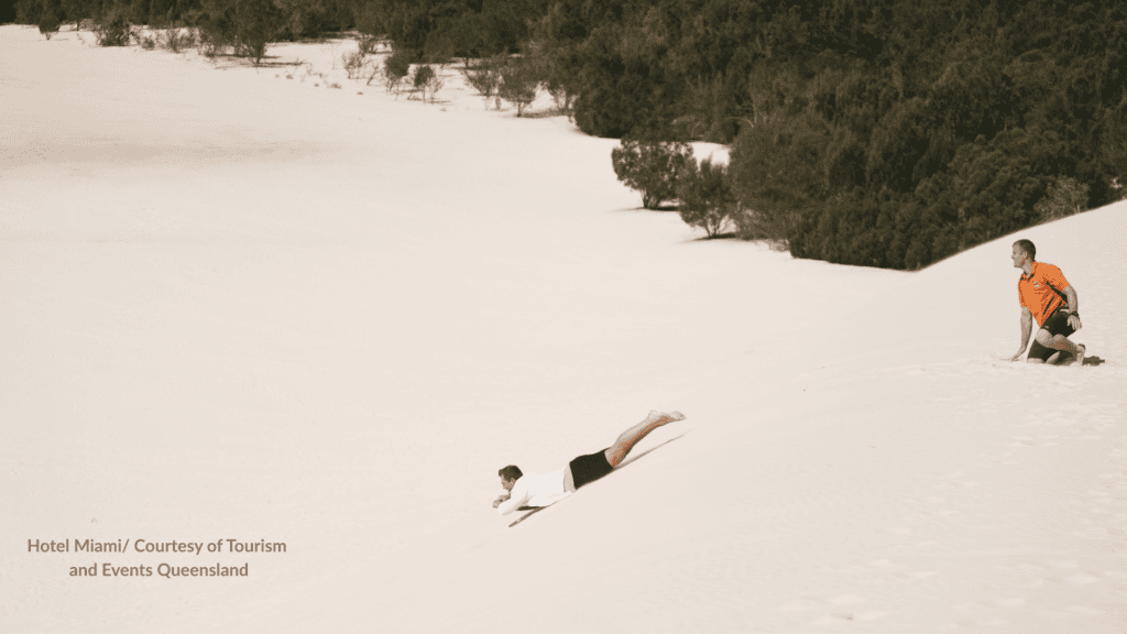 Sand tobogganing on the desert dunes at Moreton Island Queensland with a guide on the slope