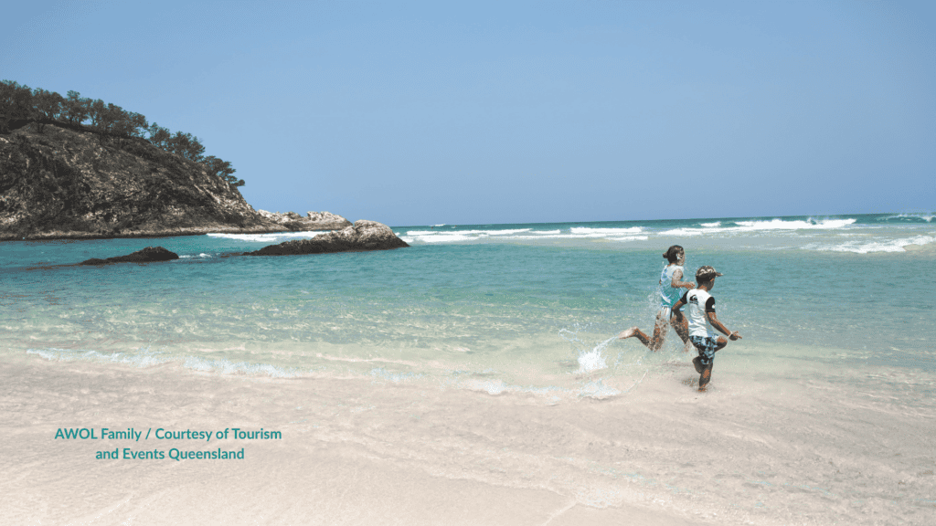 Kids running through the shallows swimming at Main Beach Stradbroke Island beside the Point Lookout headland Queensland