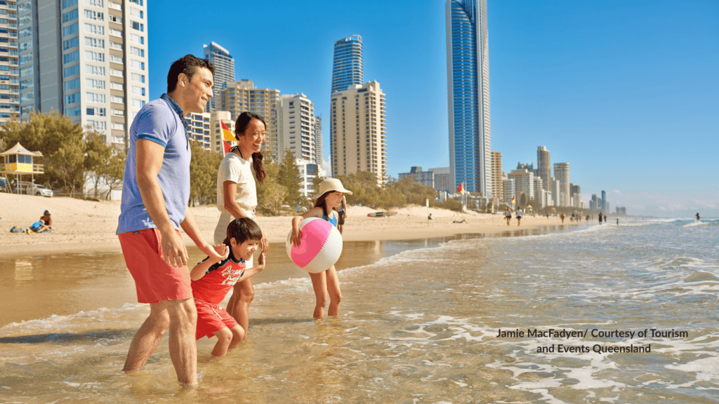 Family walking in the shallows at Surfers Paradise Beach with the Gold Coast Queensland skyline behind