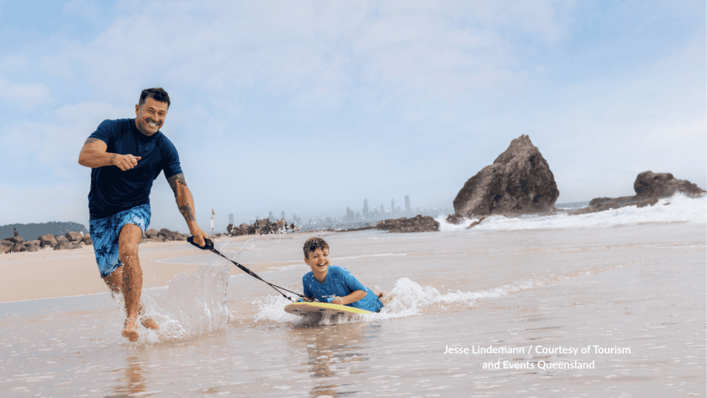 Father pulling a child on a bodyboard at Currumbin Beach Gold Coast Queensland in front of Elephant Rock