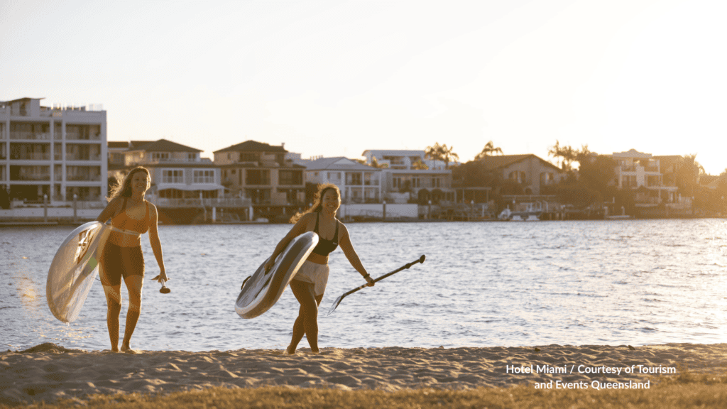 Two women carrying paddleboards at sunset at Budds Beach Gold Coast Queensland on the Nerang River