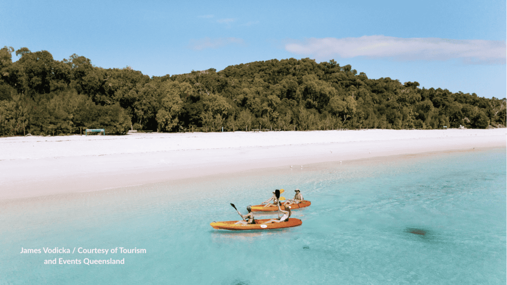 People kayaking in clear turquoise water off the white silica sand of Whitehaven Beach on Whitsunday Island Queensland