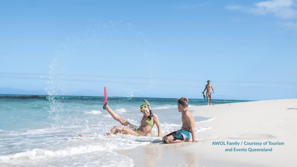 Child in a snorkel mask and fin splashing in the shallows with family on Vlasoff Cay Queensland