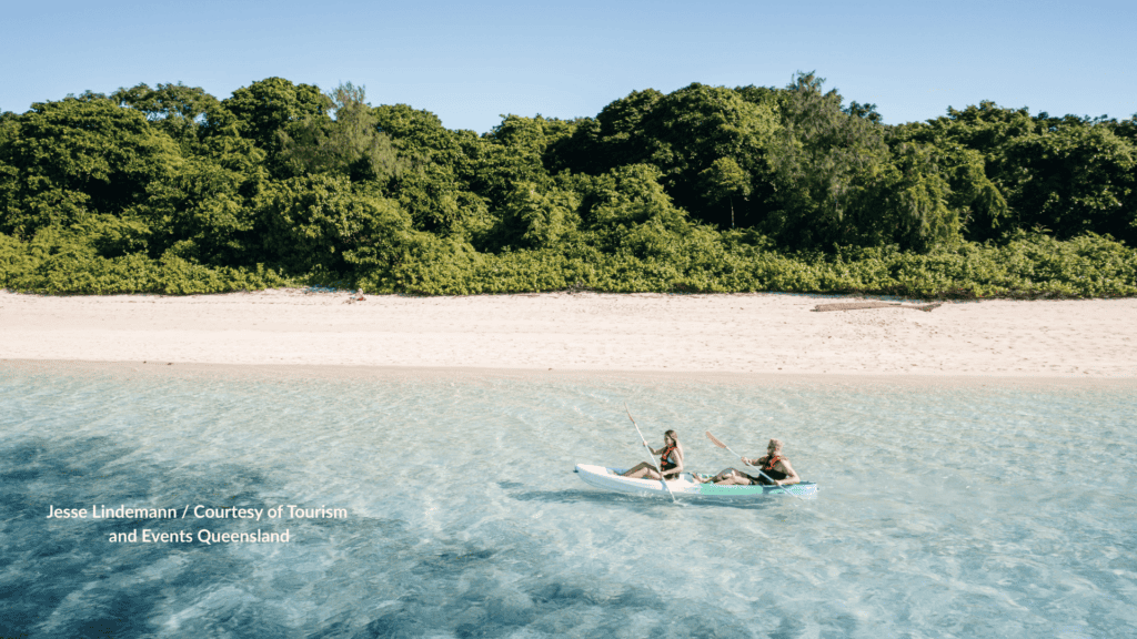 Two people kayaking in clear shallow water off the white sand beach at Green Island Queensland