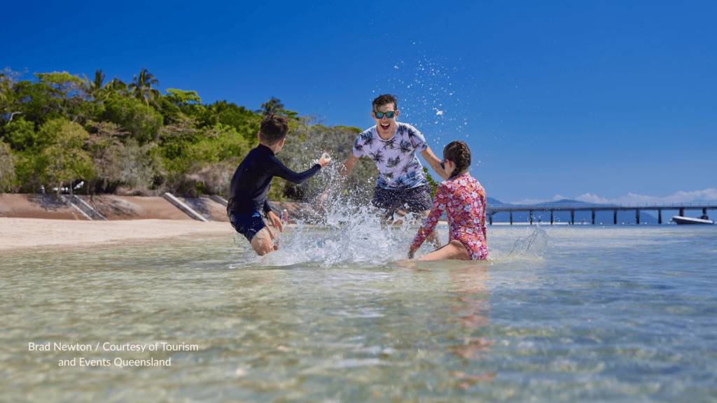 Family splashing in the shallow water at Green Island Queensland with the jetty behind