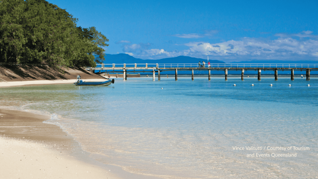 Queensland Green Island jetty over clear shallow water with the beach and a small boat on the sand