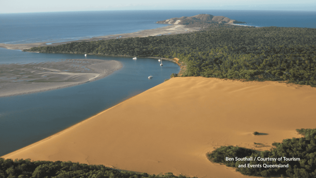 Curtis Island Yellow Patch sand blow beside the channel with boats and forested headland Queensland