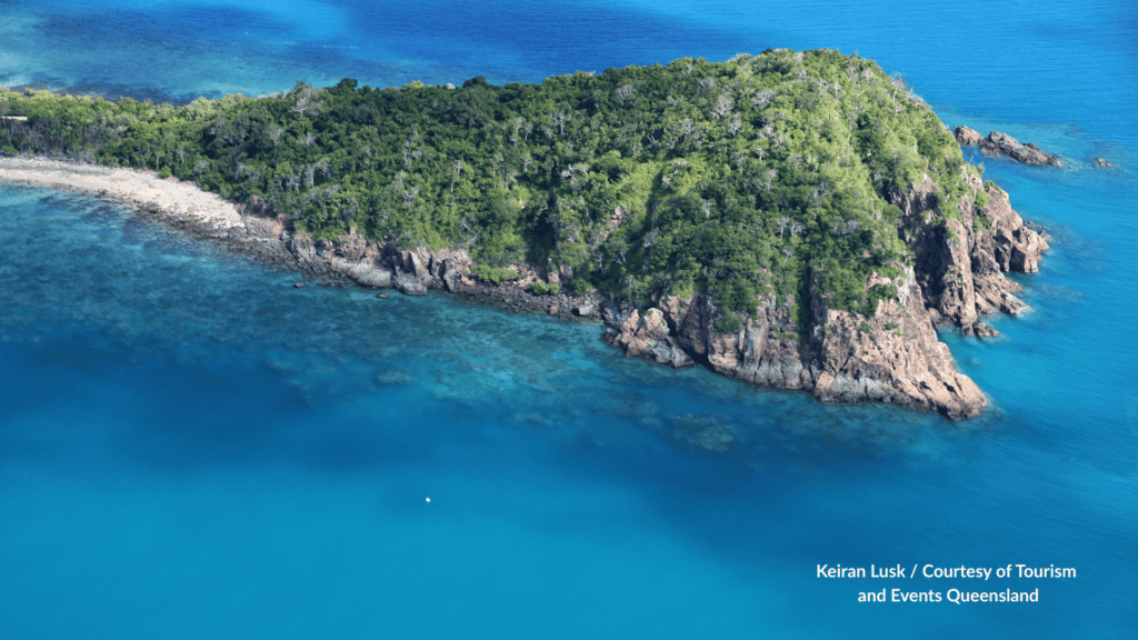 Aerial view of Langford Island in the Whitsundays Queensland showing the forested cay, rocky shoreline, white sand beach and clear turquoise water