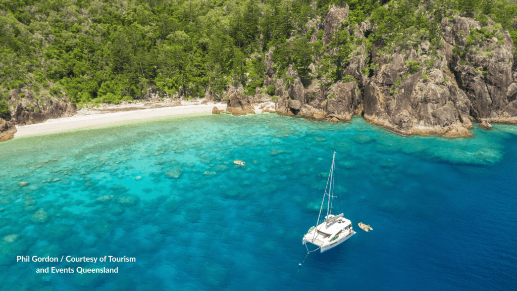 Aerial view of Manta Ray Bay on Hook Island in the Whitsundays Queensland with a white sand beach, rocky headland, turquoise reef water and a catamaran at anchor